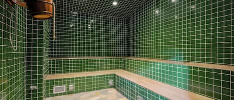 A green-tiled bathroom with a wooden bench and a hanging light fixture.