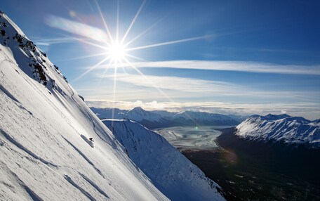 A snow-covered mountain slope with a clear sky and distant mountains.