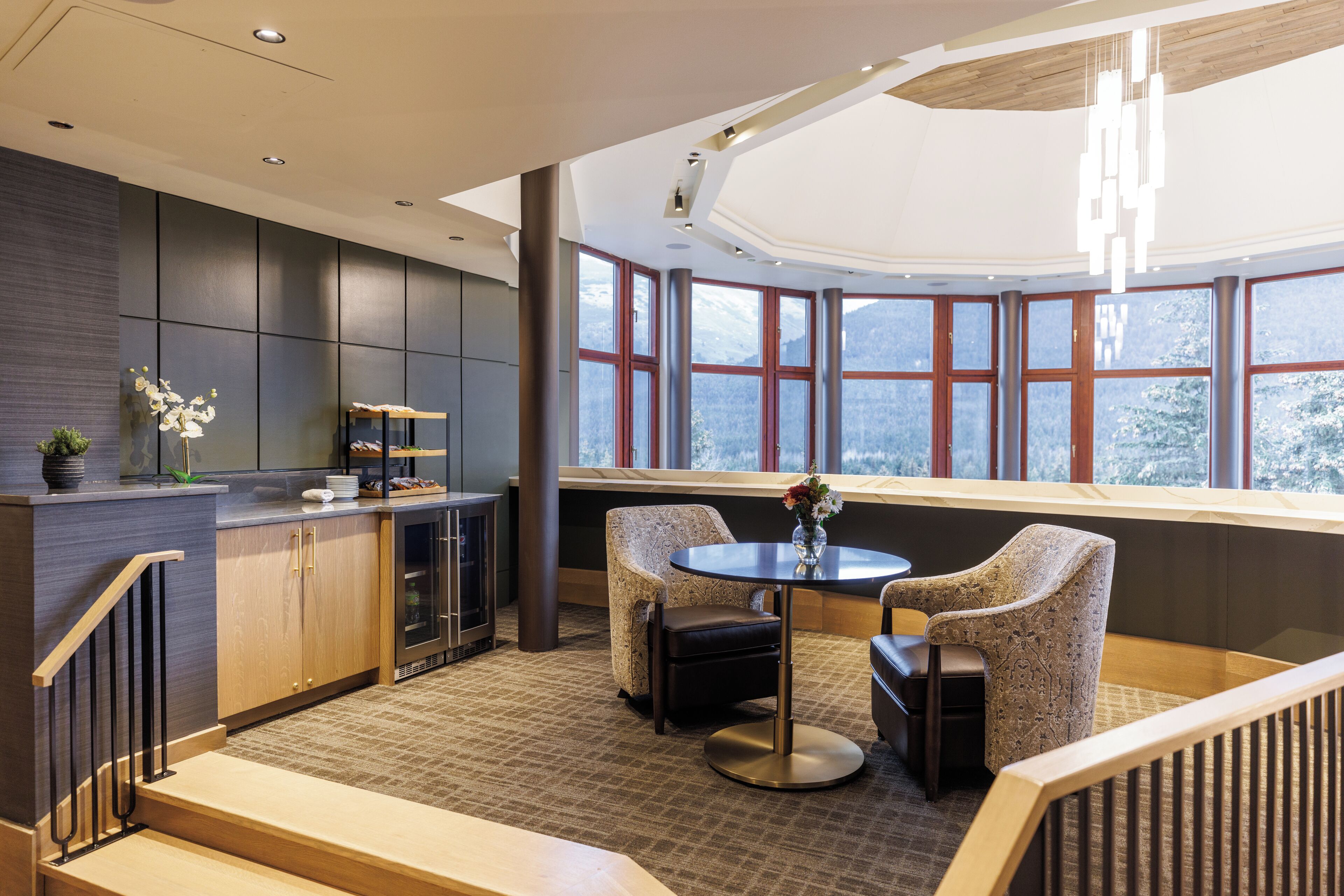 A modern interior with a kitchen area, seating by a large window, and a staircase.