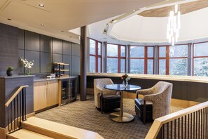 A modern interior with a kitchen area, seating by a large window, and a staircase.