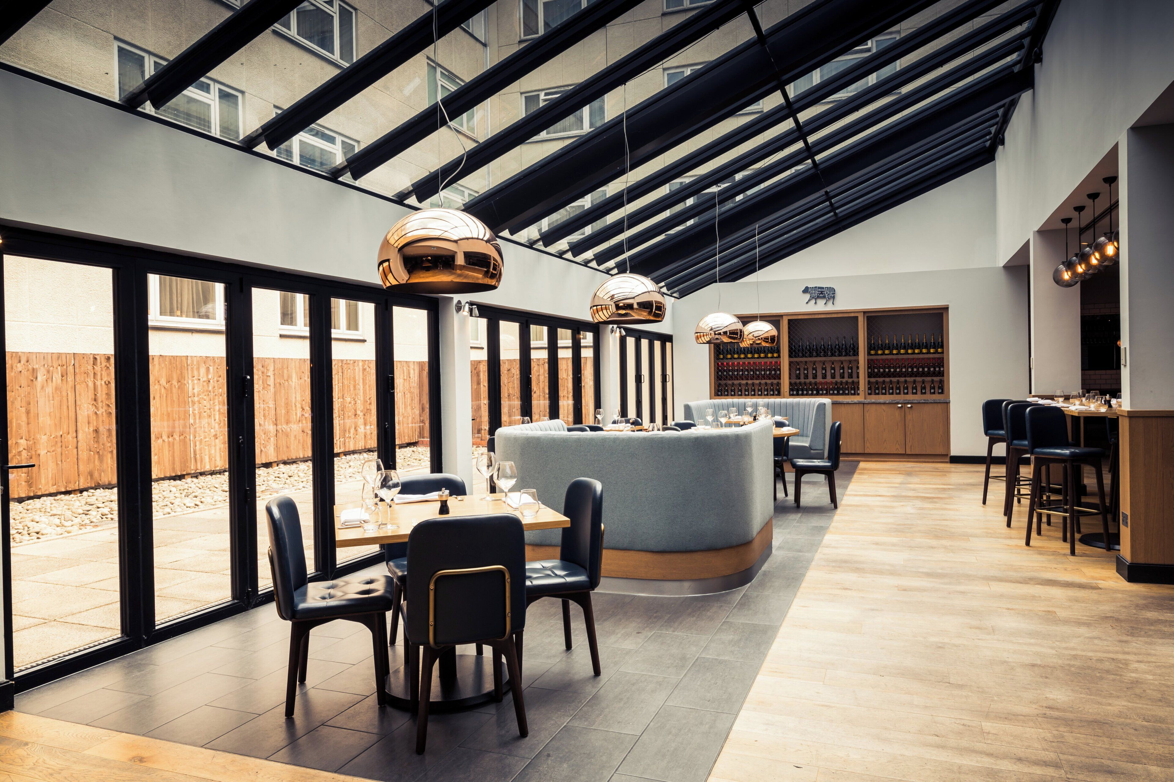 A modern restaurant with a high ceiling, large windows, and a central seating area with tables and chairs.