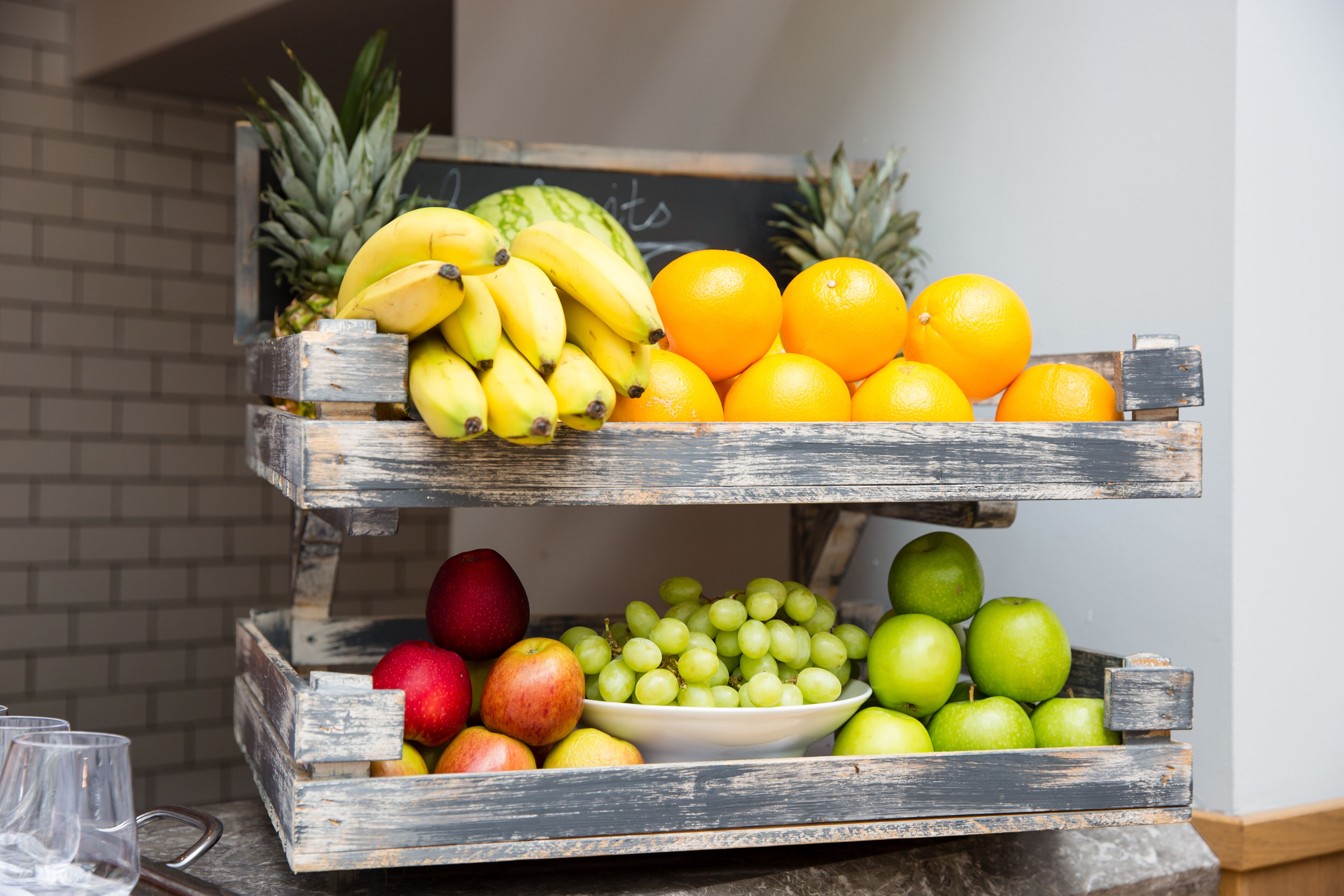 A wooden fruit stand with bananas, oranges, apples, and grapes.