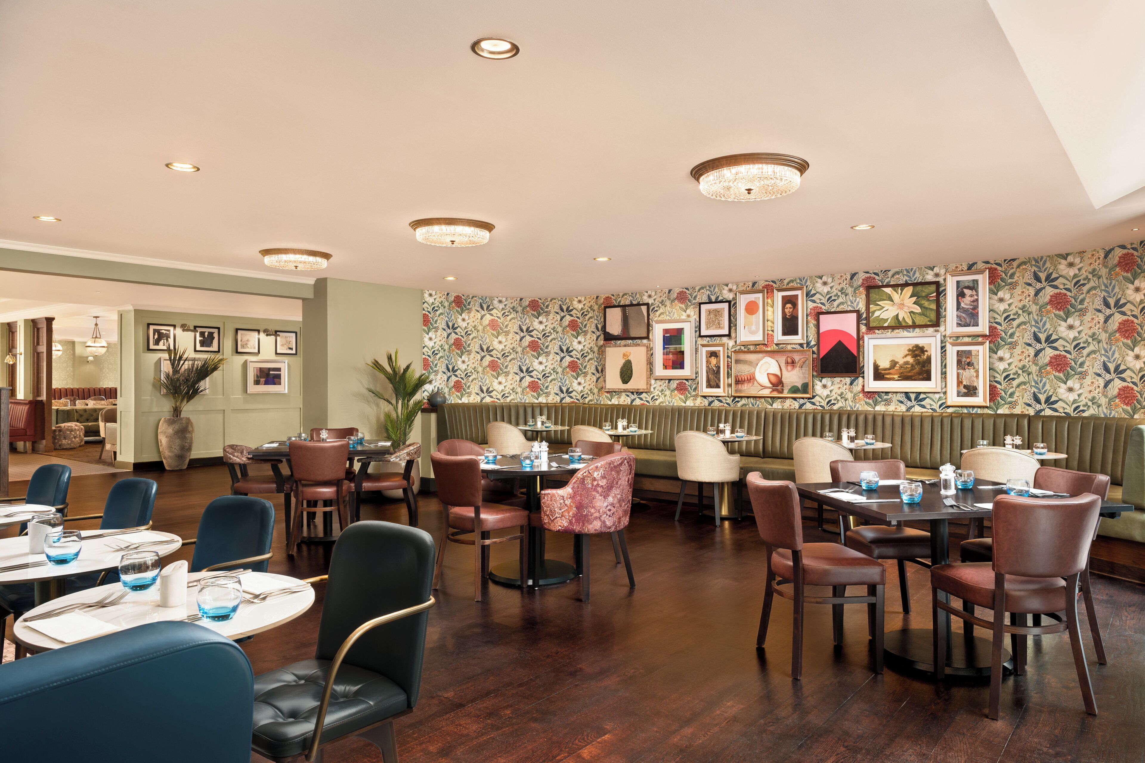 A restaurant with multiple dining tables and chairs, a patterned wall, and ceiling lights.