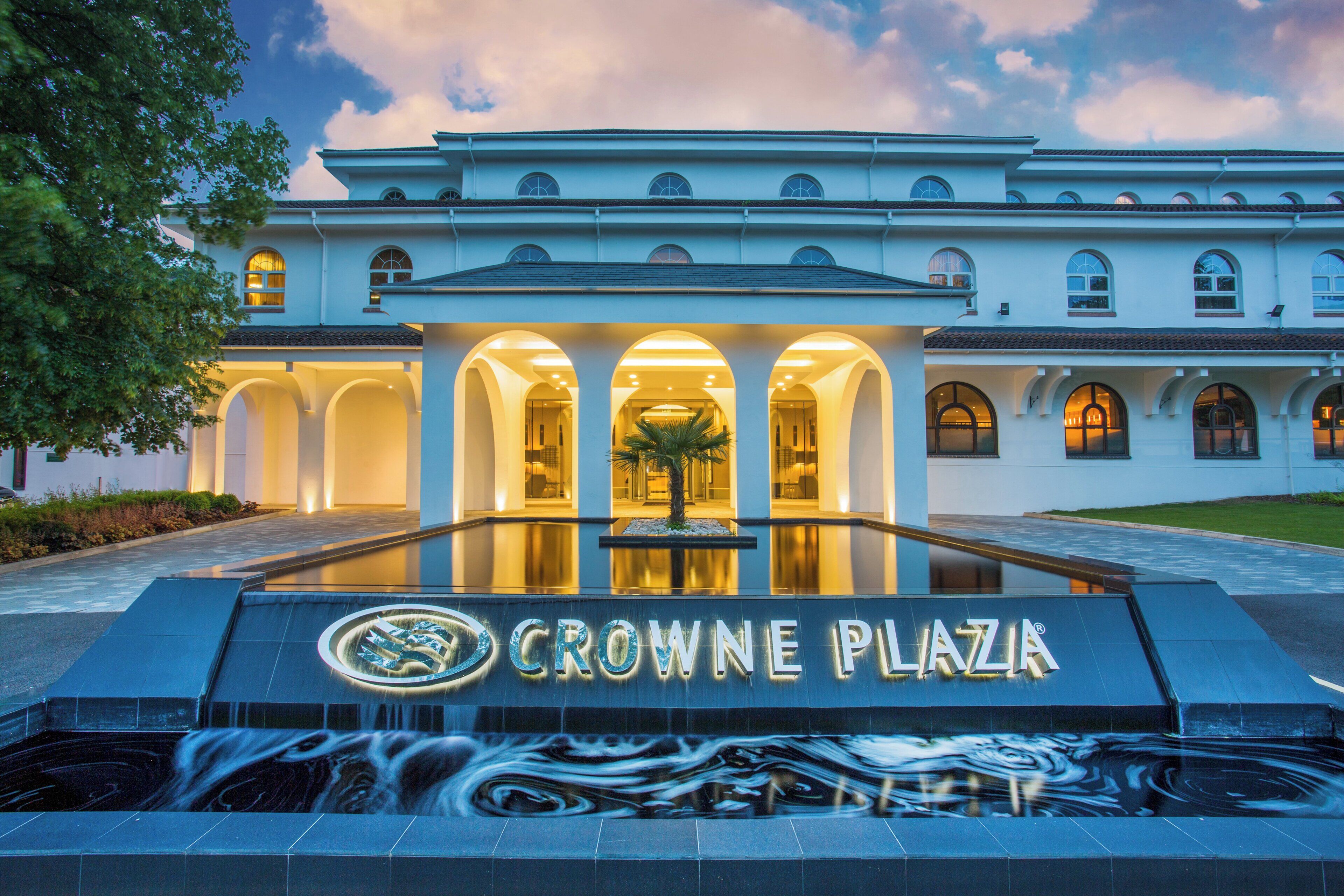 Un edificio con entrada central, columnas en arco y un letrero que dice 'CROWNE PLAZA'.
