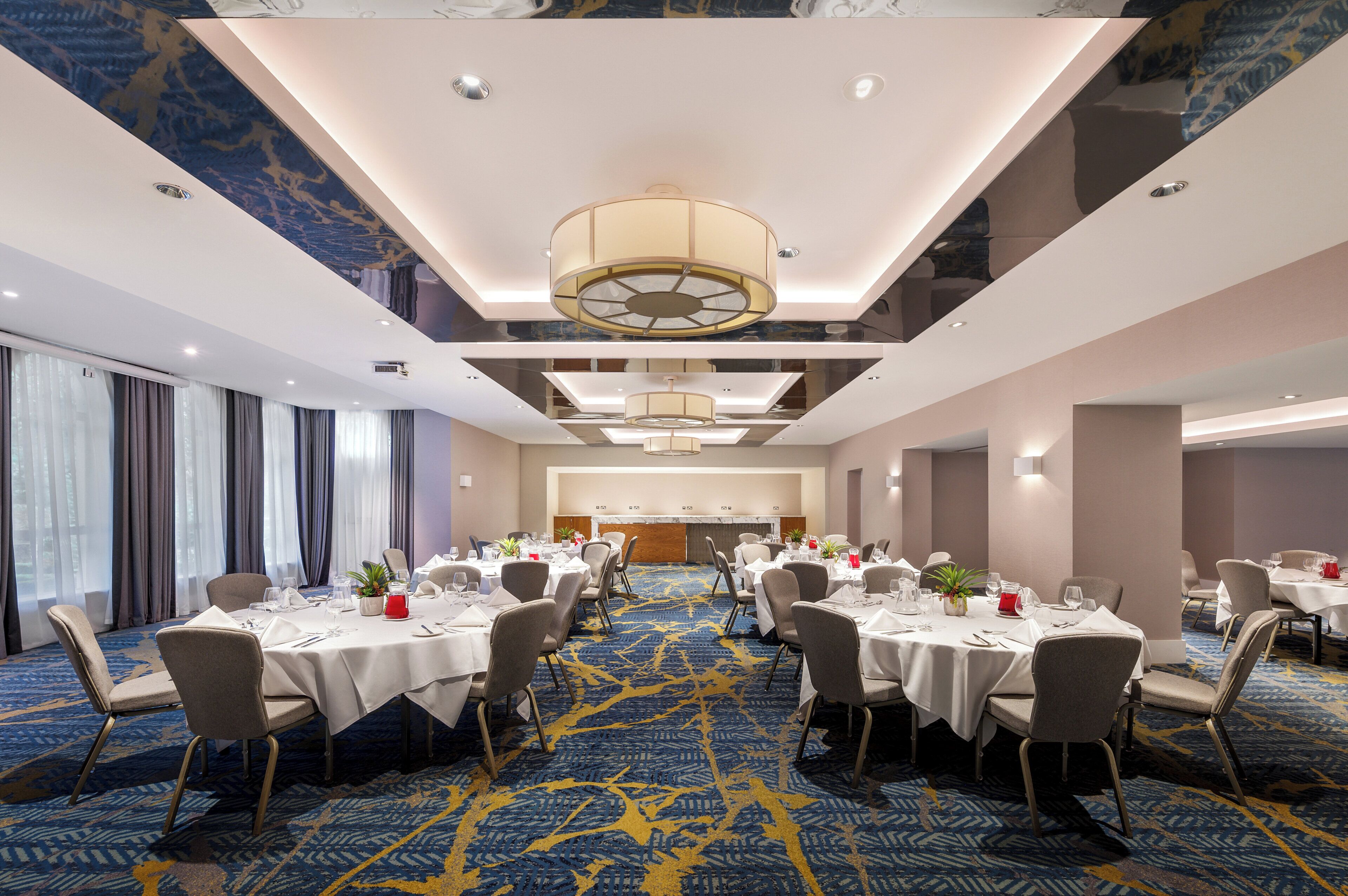 Una sala conferenze con diversi tavoli e sedie, un tappeto decorato e un soffitto con illuminazione a incasso.