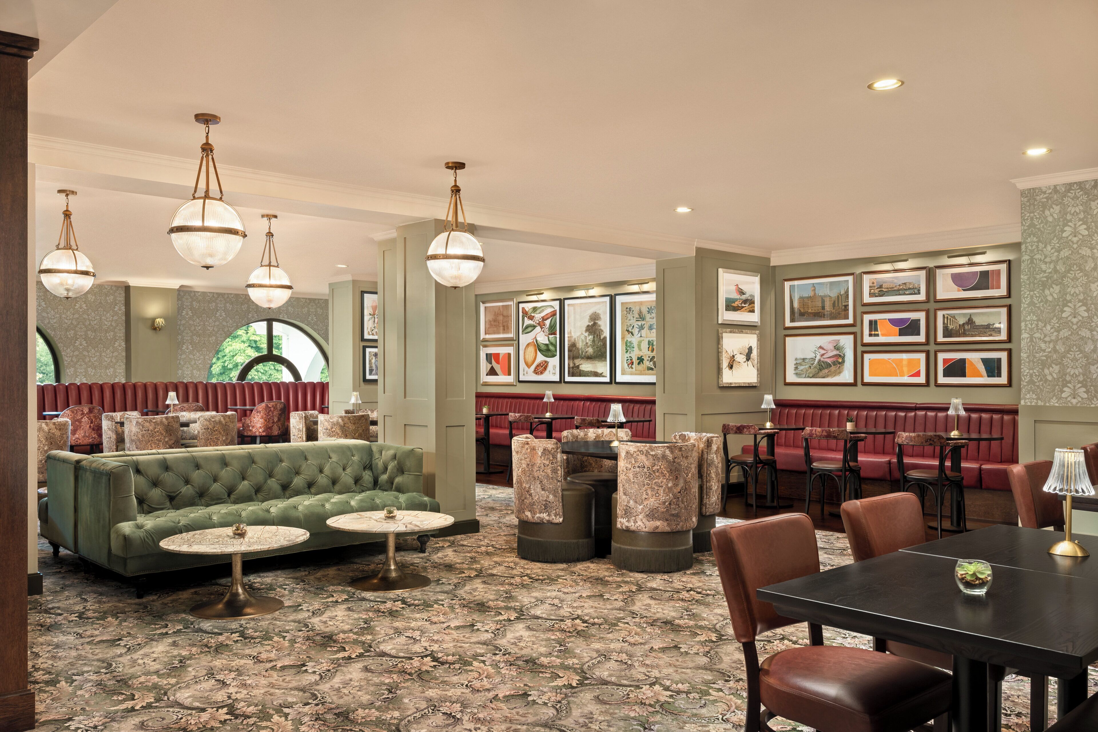 A hotel lobby with a green sofa, round tables, and a red booth area.