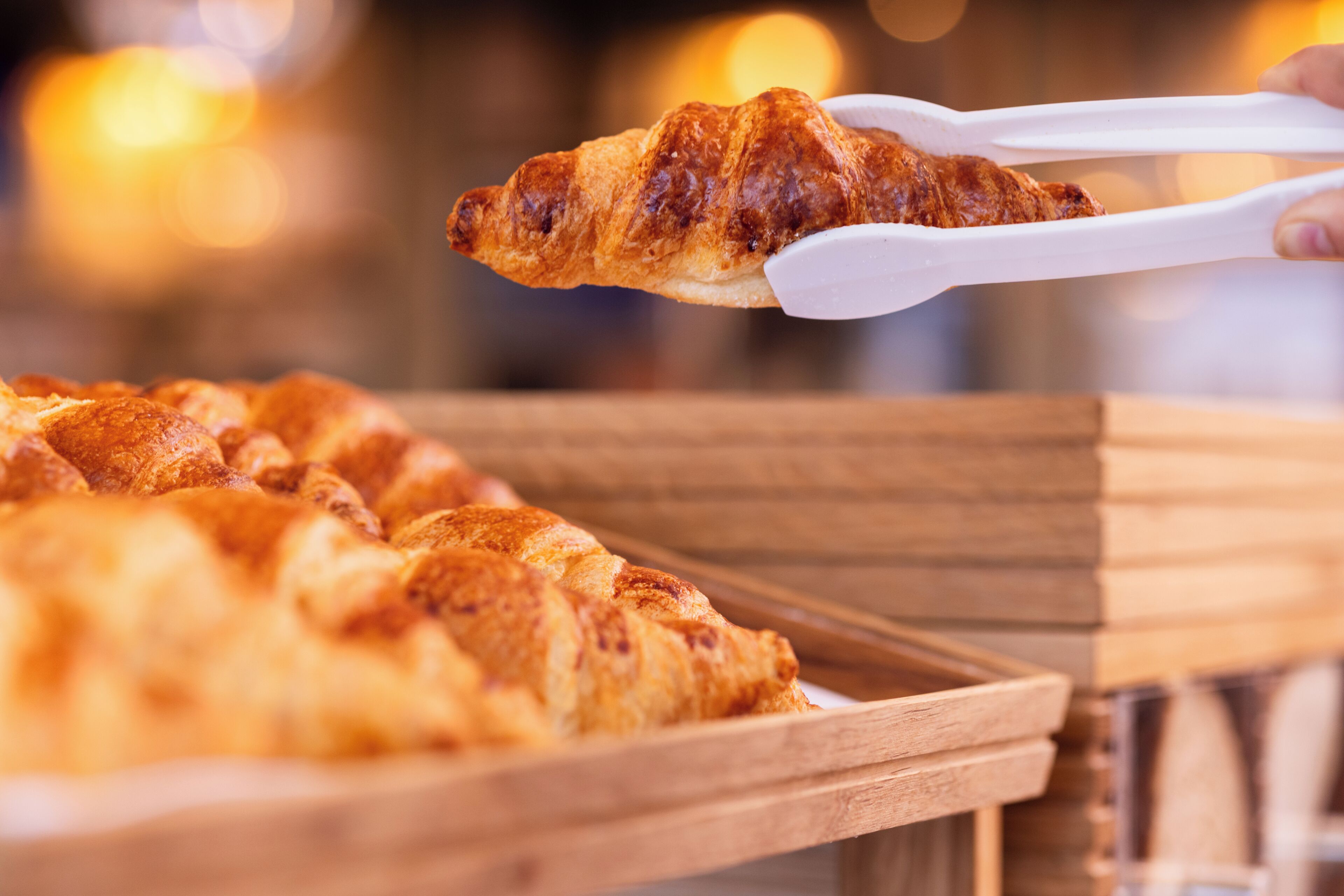 A tray of golden-brown pastries, likely croissants, being held by tongs.