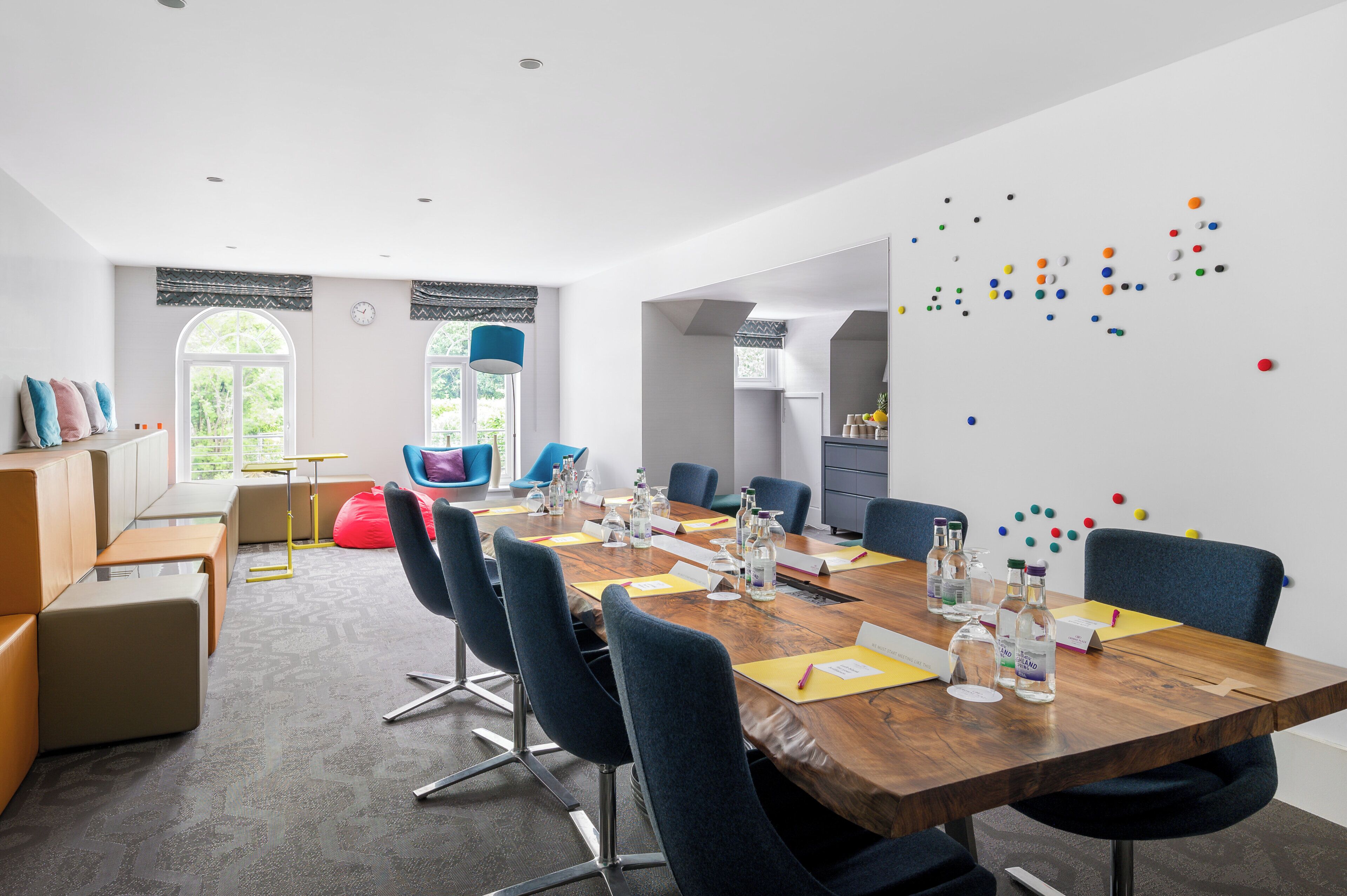 A modern conference room with a long table, chairs, and a whiteboard with colorful dots.