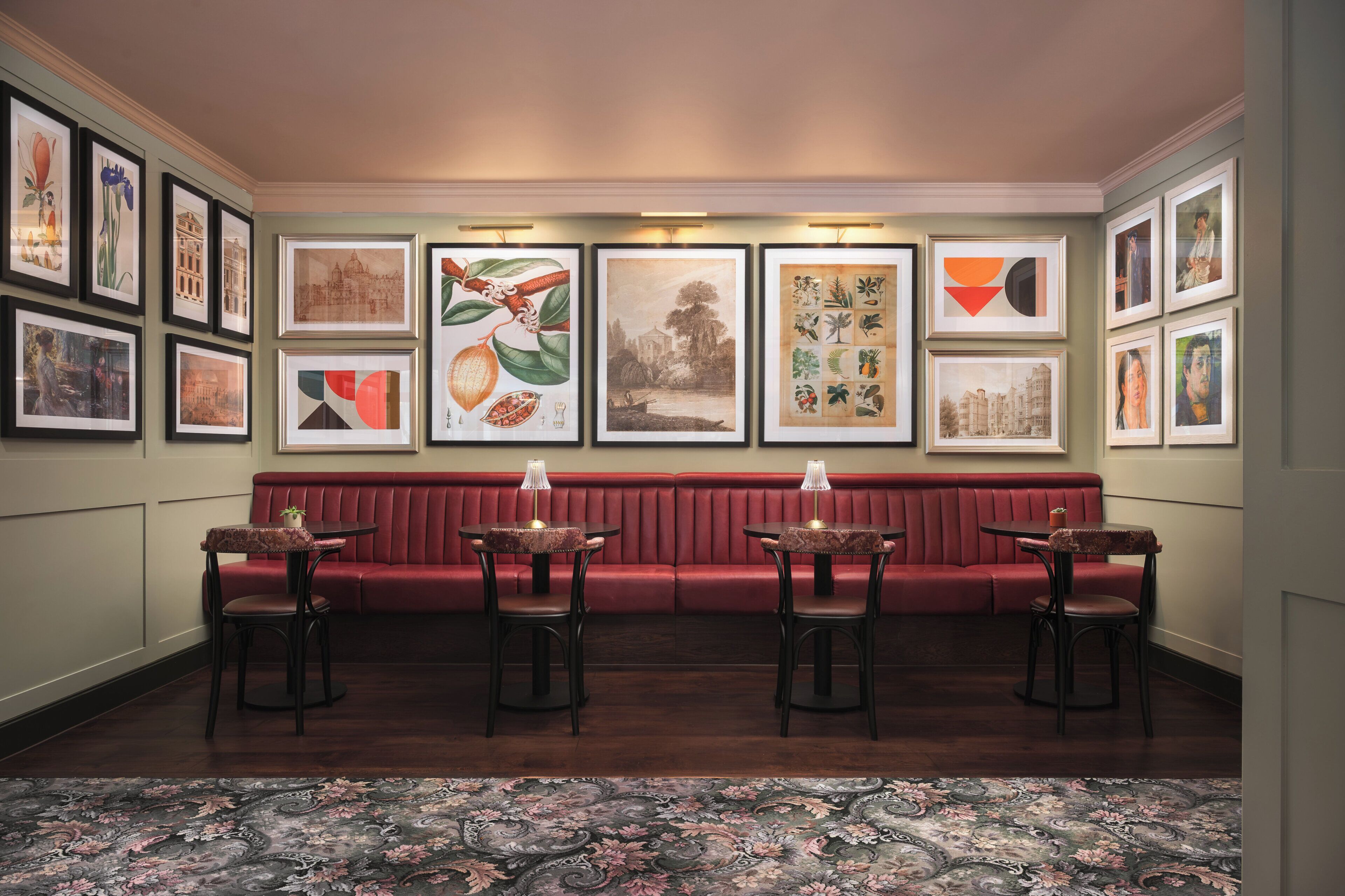 A room with a red cushioned bench, four tables with lamps, and framed artwork on the walls.