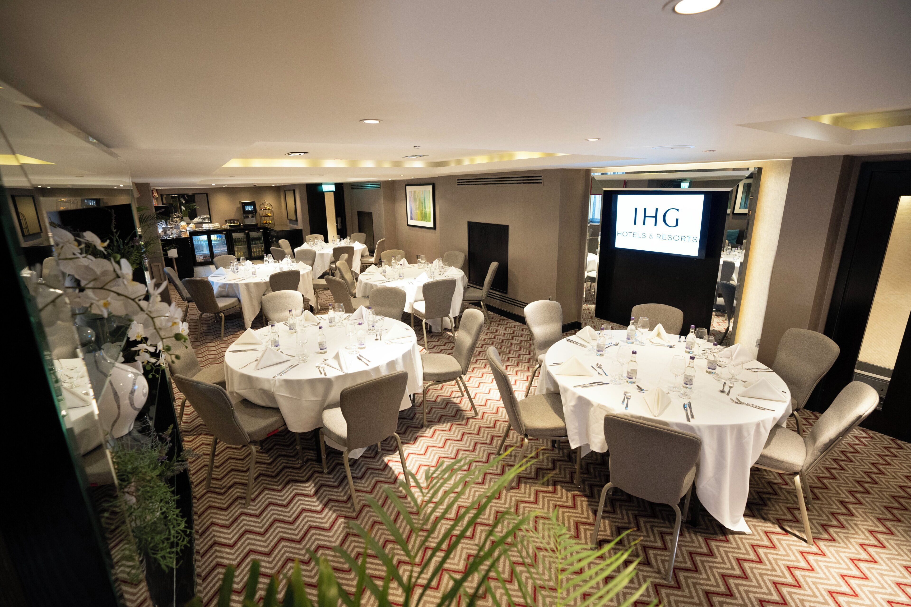 A hotel conference room with multiple round tables set for dining, equipped with chairs and table settings.