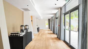 Un pasillo de hotel con una estación de café, puertas numeradas y ventanas amplias.