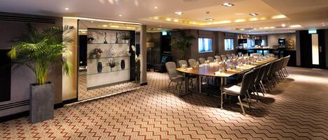 A conference room with a long table, chairs, and a patterned carpet.