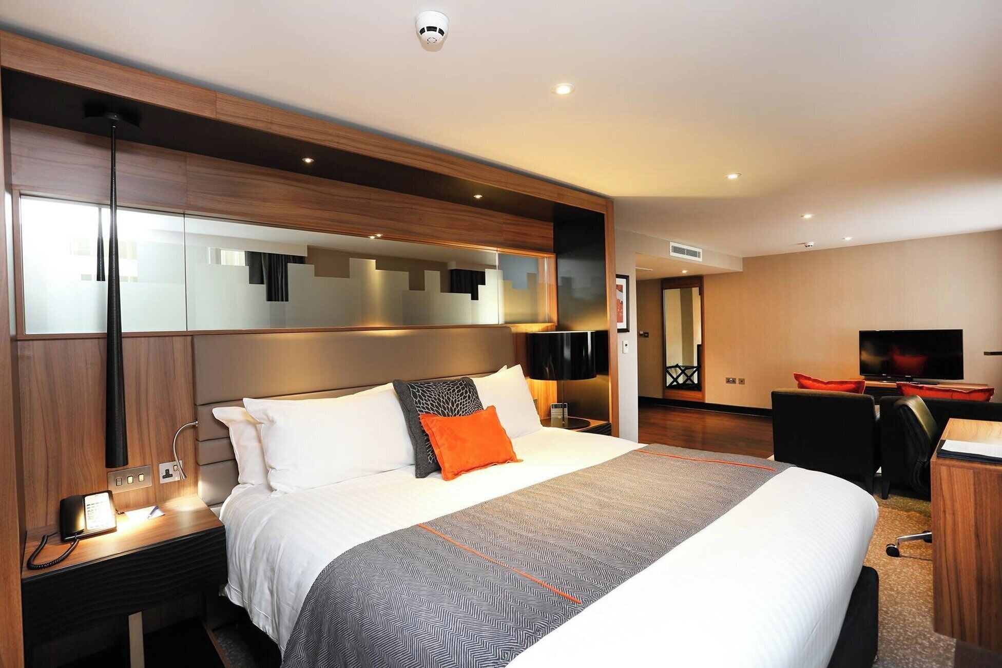 A hotel room with a bed, bedside table, lamp, and a television.