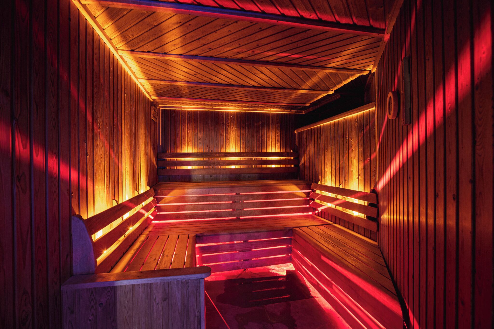 Eine Sauna mit Holzwänden und -bänken, beleuchtet durch rotes Licht.
