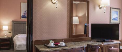 A hotel room with a bed, a desk with a flat-screen TV, a chair, and a mirror.