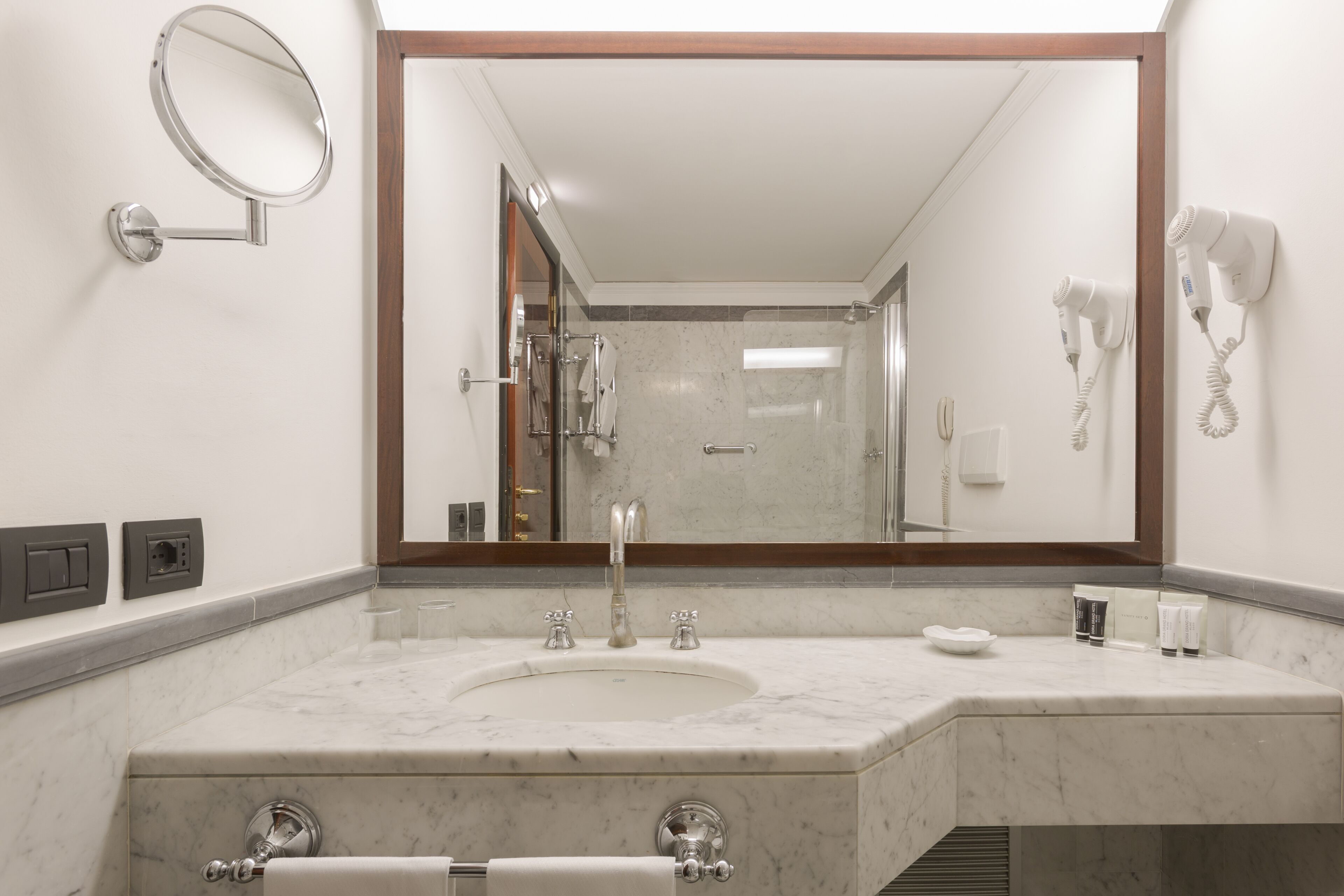 A modern bathroom with a large mirror, a sink with two faucets, and a hairdryer mounted on the wall.