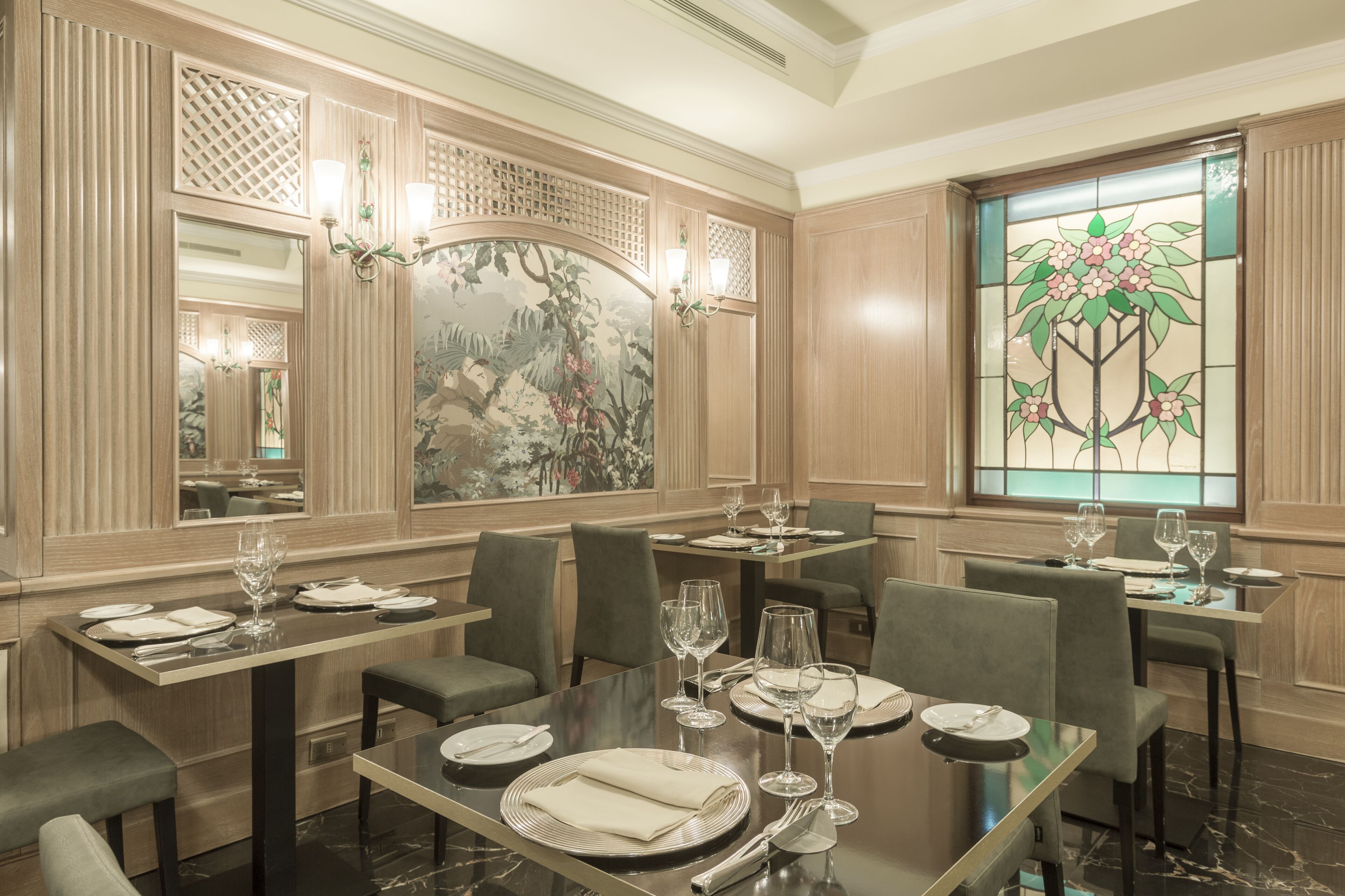 A dining area with wooden paneling, a large floral stained glass window, and multiple tables set for dining.