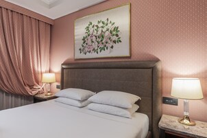 A hotel room with a bed, two bedside lamps, a nightstand, a painting of flowers, and a curtain.
