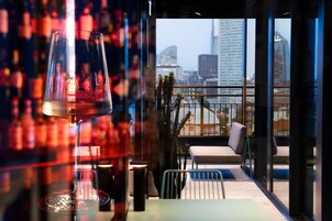 A modern bar area with a glass table, a glass with a drink, and a view of a cityscape through large windows.