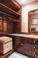 A wooden vanity with a mirror, a hanging coat rack, and a cushioned stool.
