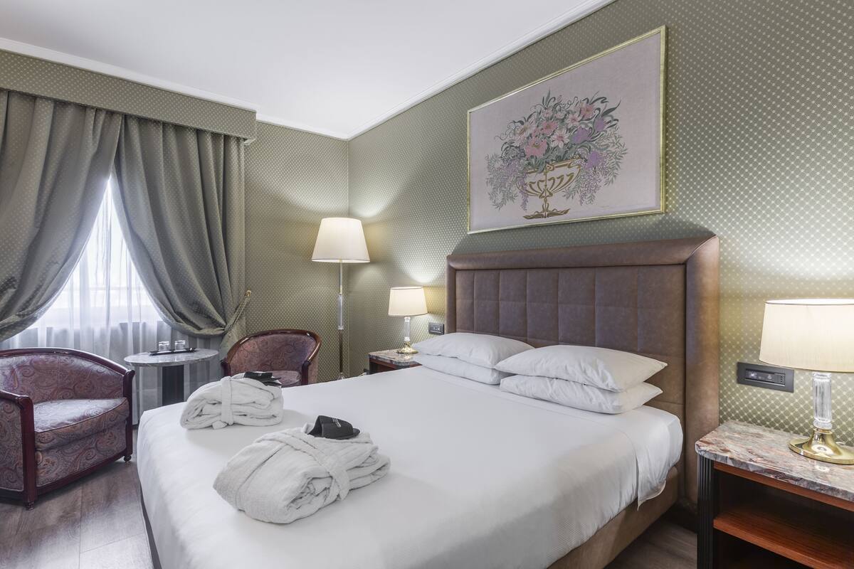A hotel room with a large bed, two bedside tables, a chair, a lamp, and a painting on the wall.