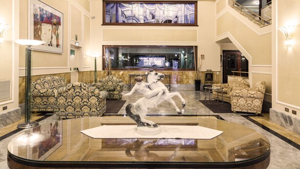 A lobby with a glass coffee table, patterned sofas, a horse sculpture, and a staircase. - Doria Grand Hotel (Milan)