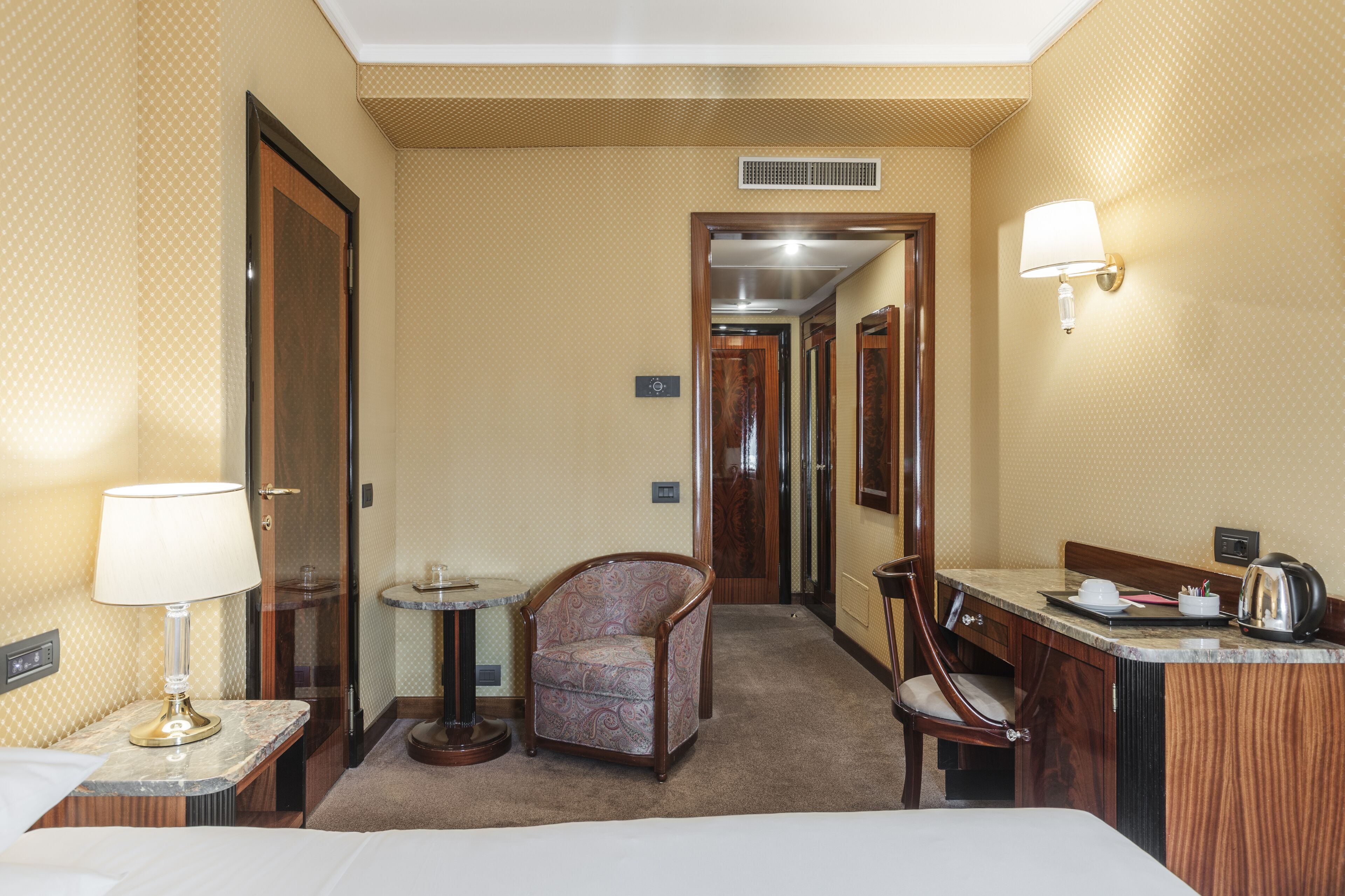 Une chambre d’hôtel comprenant un lit, un bureau avec une lampe, une chaise, une petite table et un miroir.