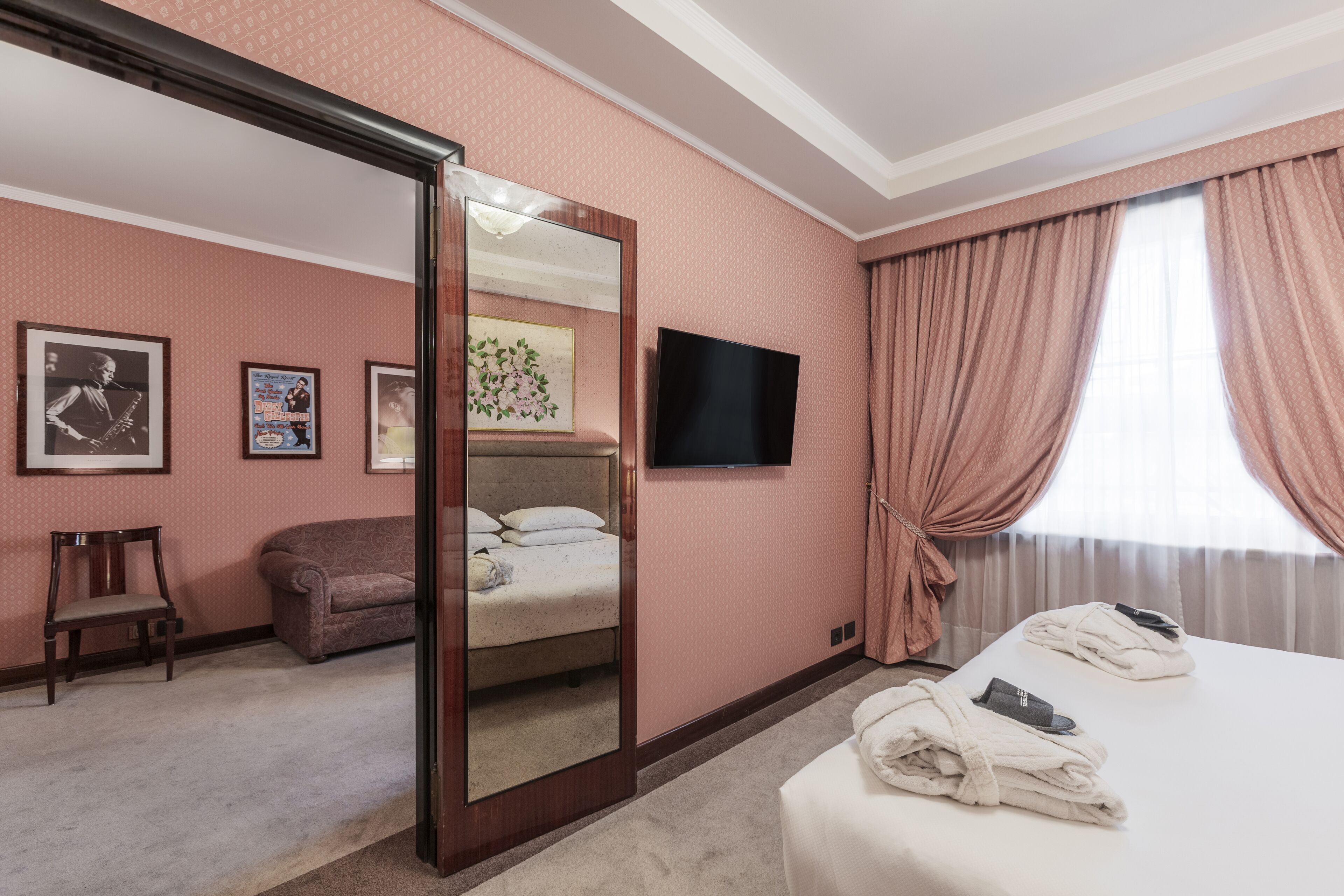 A hotel room with a bed, a chair, a sofa, a TV, and a mirror.