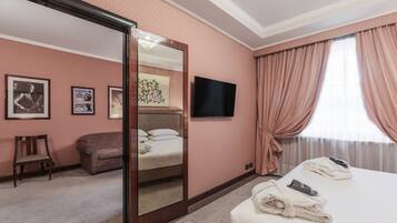 Una habitación de hotel con cama, sillón, sofá, televisor y espejo.