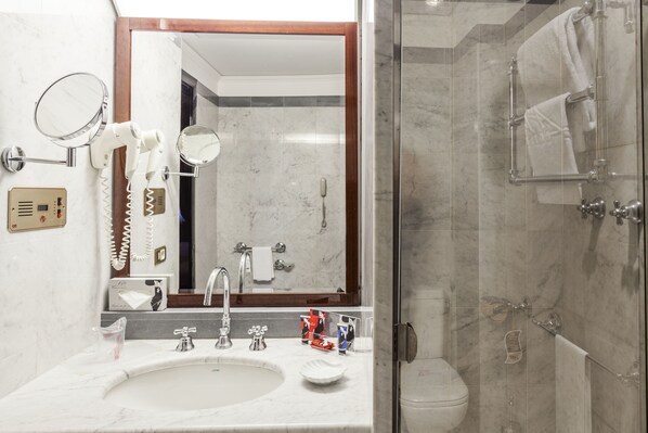 A bathroom with a sink, mirror, hair dryer, and a glass shower enclosure. - DORIA GRAND HOTEL ROOFTOP (Milan)
