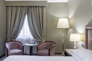 A hotel room with a bed, two armchairs, a small round table, and two lamps.