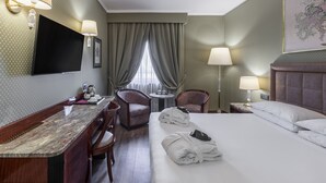 A hotel room with a bed, two chairs, a desk, a TV, and a window with curtains. - Doria Grand Hotel (Milan)