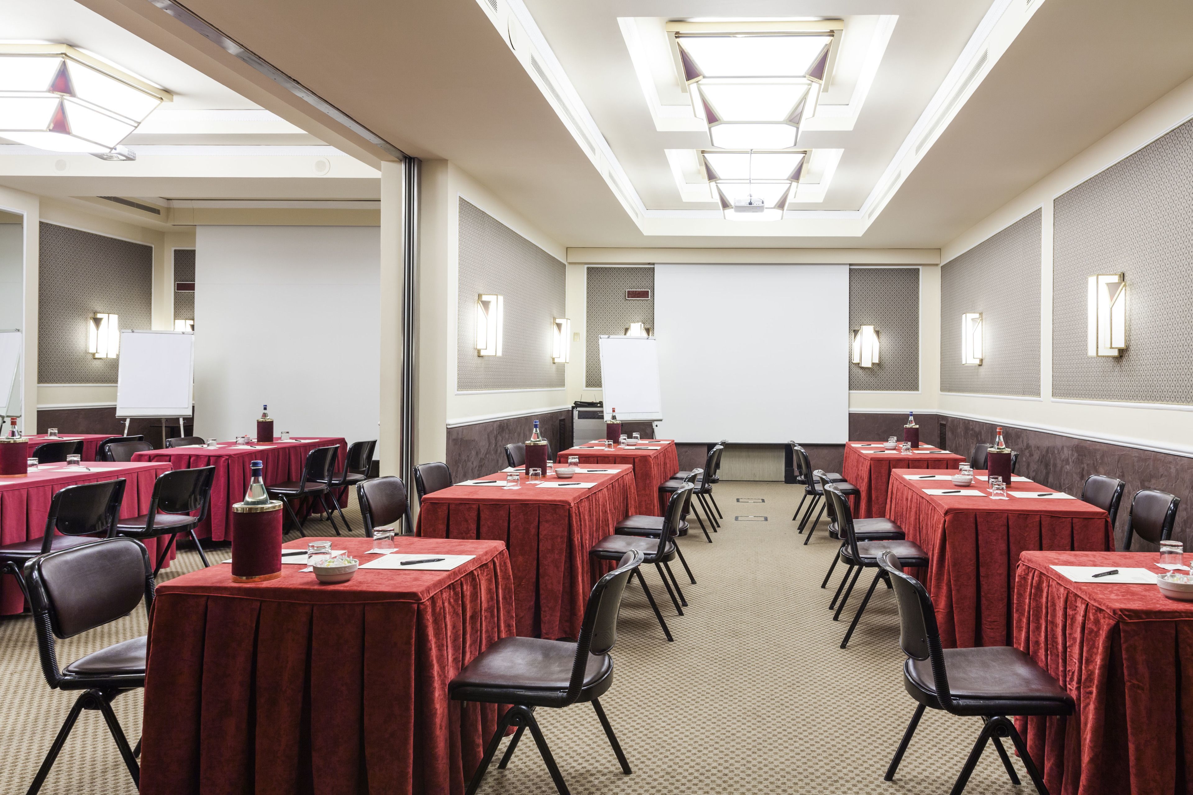 A conference room with multiple tables and chairs, equipped with presentation screens and ambient lighting.