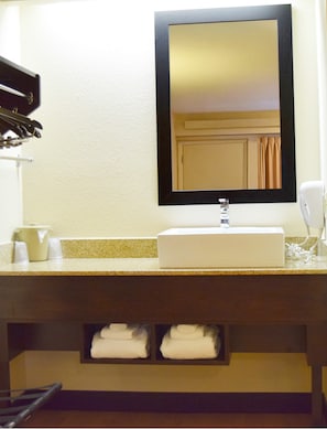 A hotel bathroom with a sink, mirror, towel rack, and a towel dispenser. - Red Roof Inn PLUS+ University at Buffalo - Amherst (Buffalo)