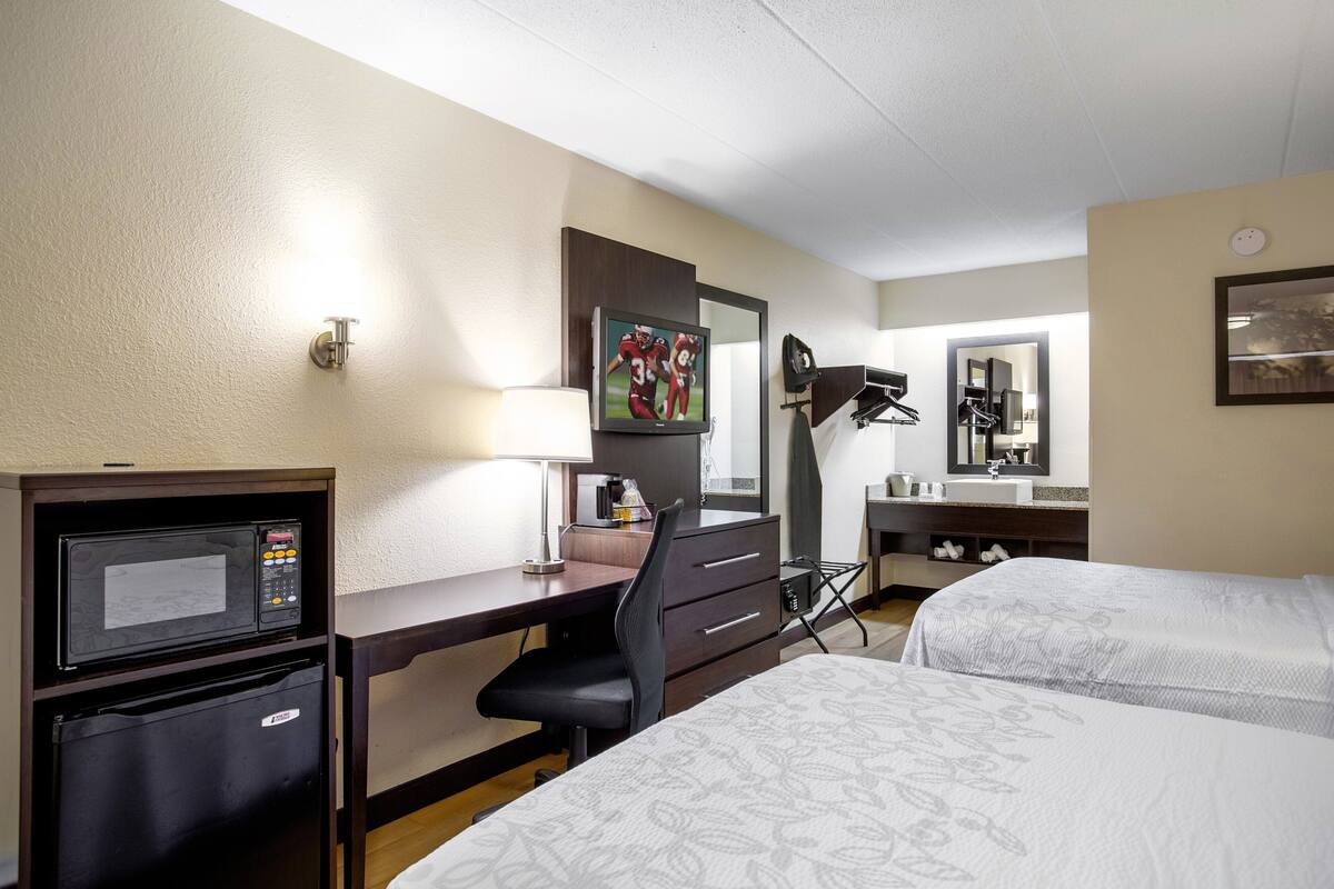 Een hotelkamer met een bureau, een magnetron, een koelkast, twee bedden, een spiegel en een televisietoestel.