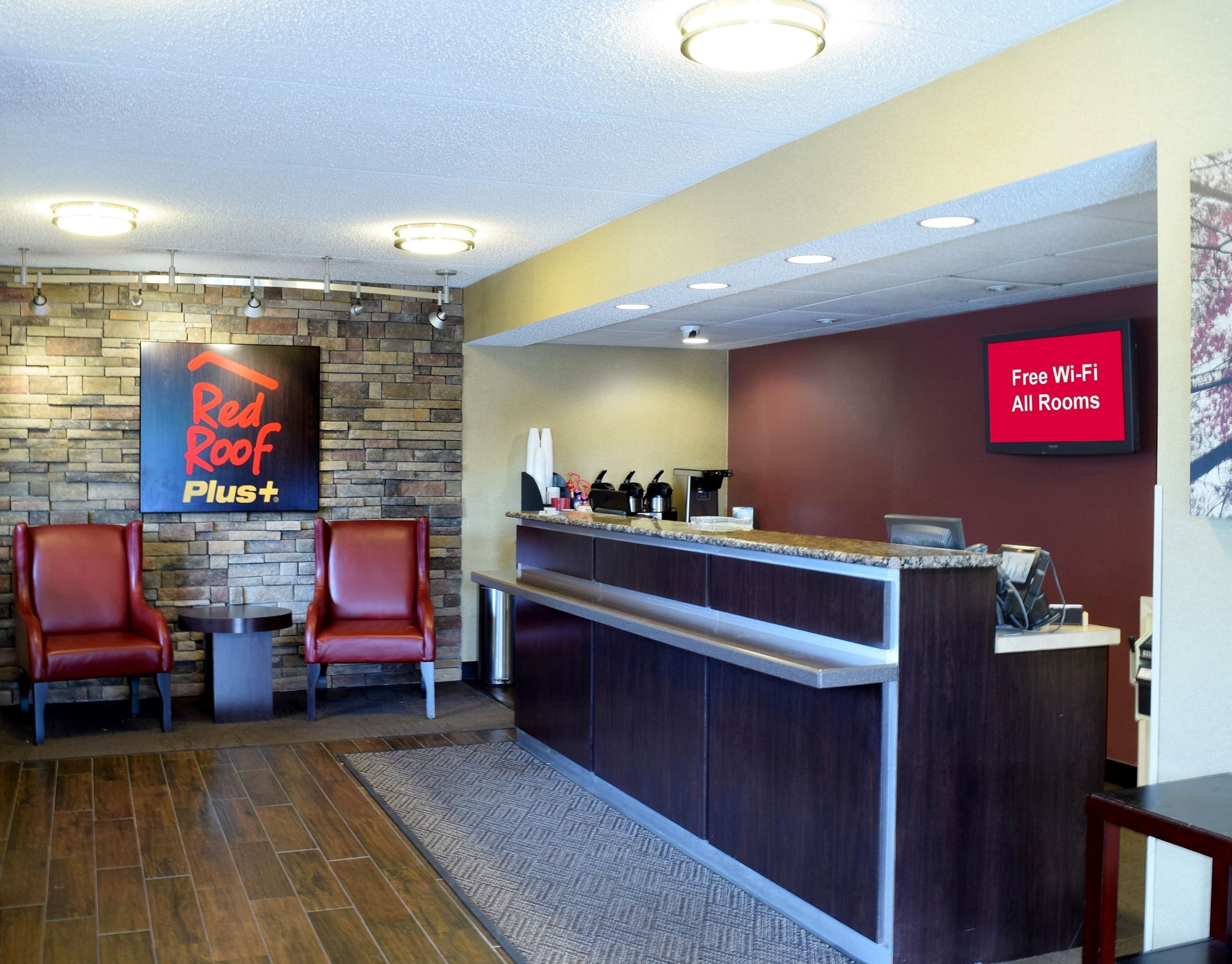 L’espace d’accueil d’un hôtel Red Roof Plus, avec un mur en pierre, deux fauteuils en cuir, un comptoir d’accueil et un panneau indiquant que le Wi-Fi est gratuit dans toutes les chambres.