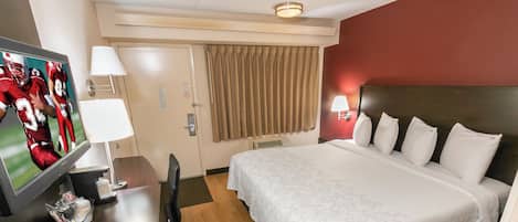 A hotel room with a bed, a desk with a television, a chair, and a window with curtains.