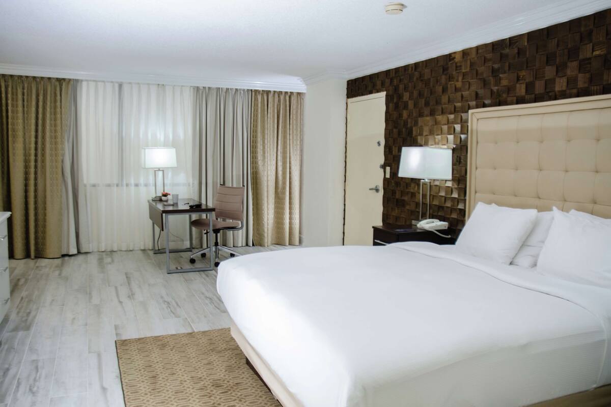 Une chambre d’hôtel avec un grand lit, un bureau avec une chaise, une lampe de bureau, un téléphone et un téléviseur fixé au mur.