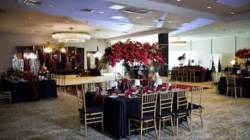 Une salle de banquet avec des tables rondes, des chaises et des centres de table floraux.