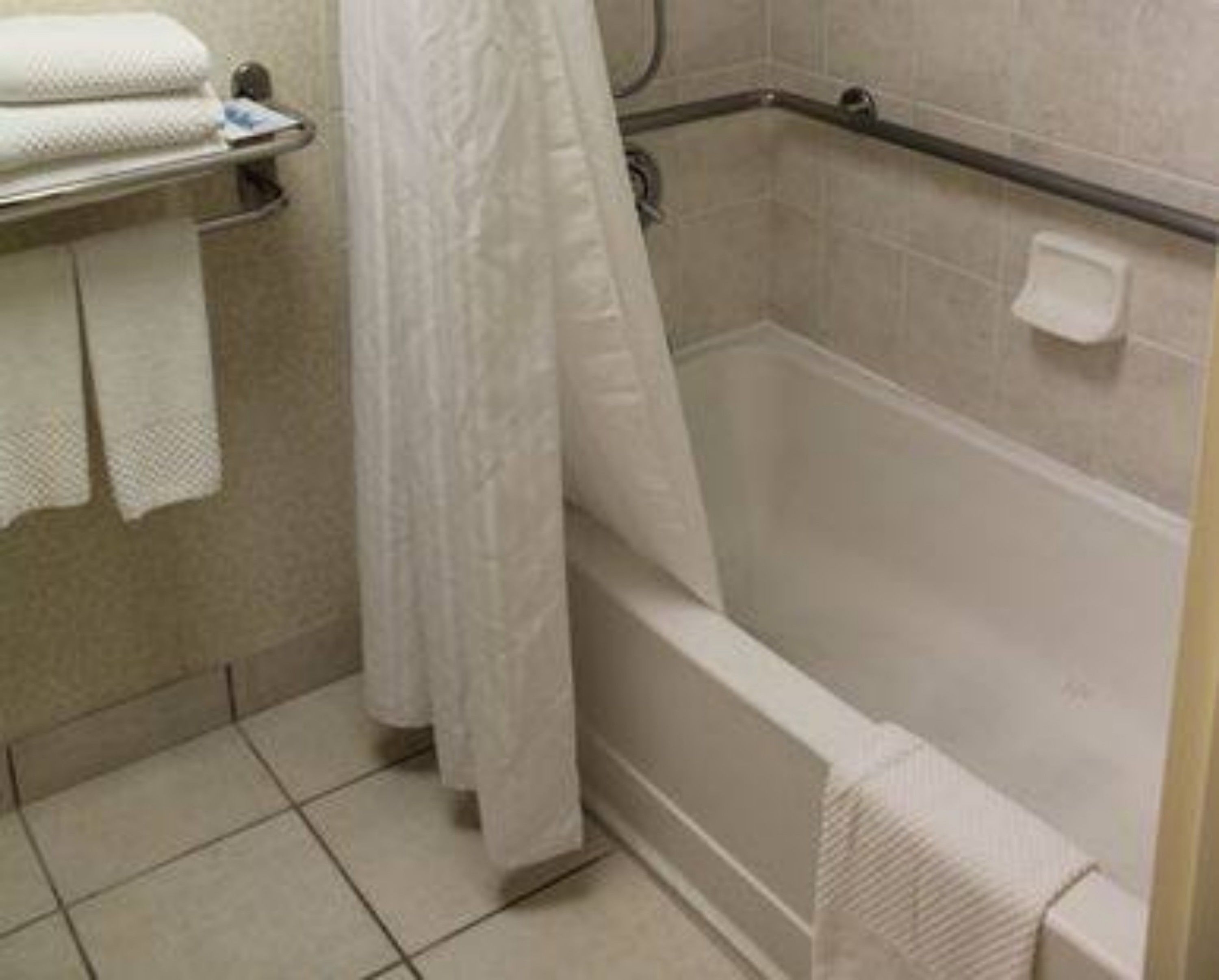 Un baño con bañera, ducha e inodoro. Hay toallas en un estante y una cortina de ducha.