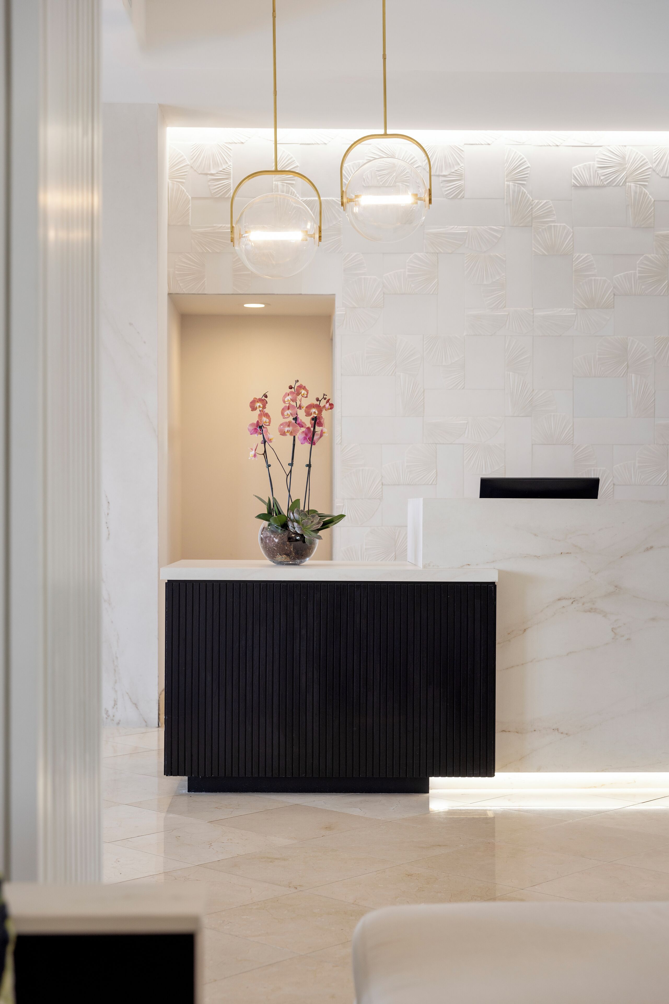 A reception area with a marble wall, a black reception desk, and a vase with flowers.