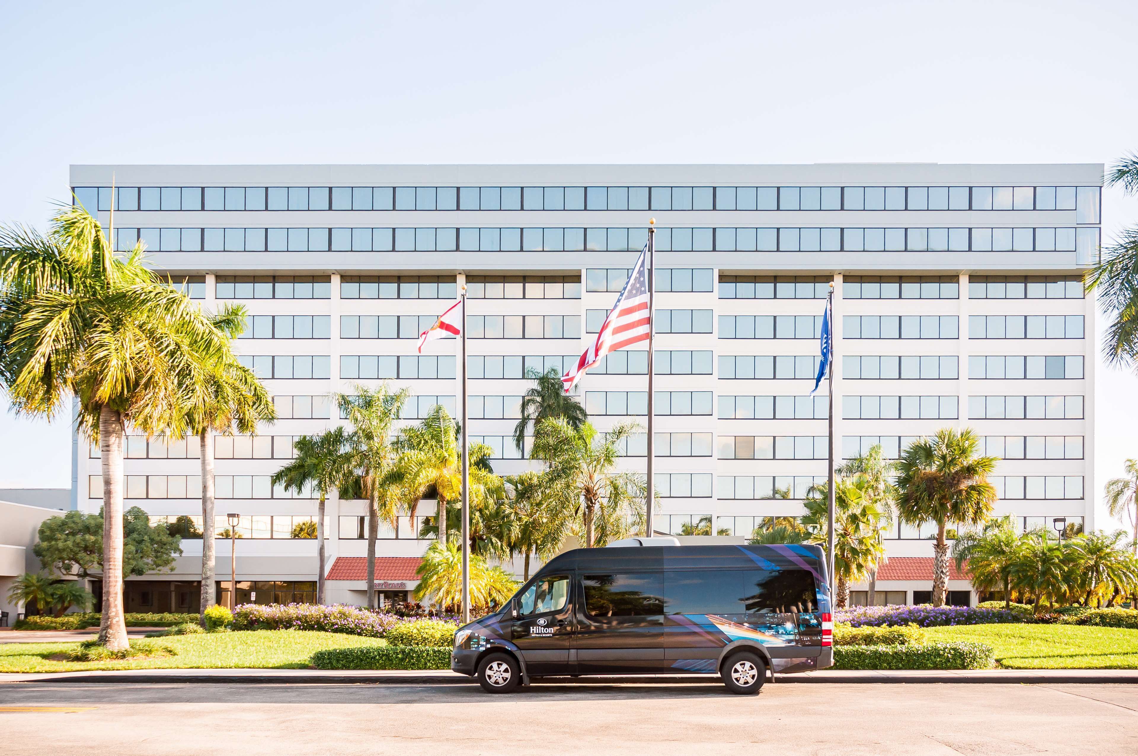 Un hotel moderno con una estructura de varios pisos, palmeras y banderas.