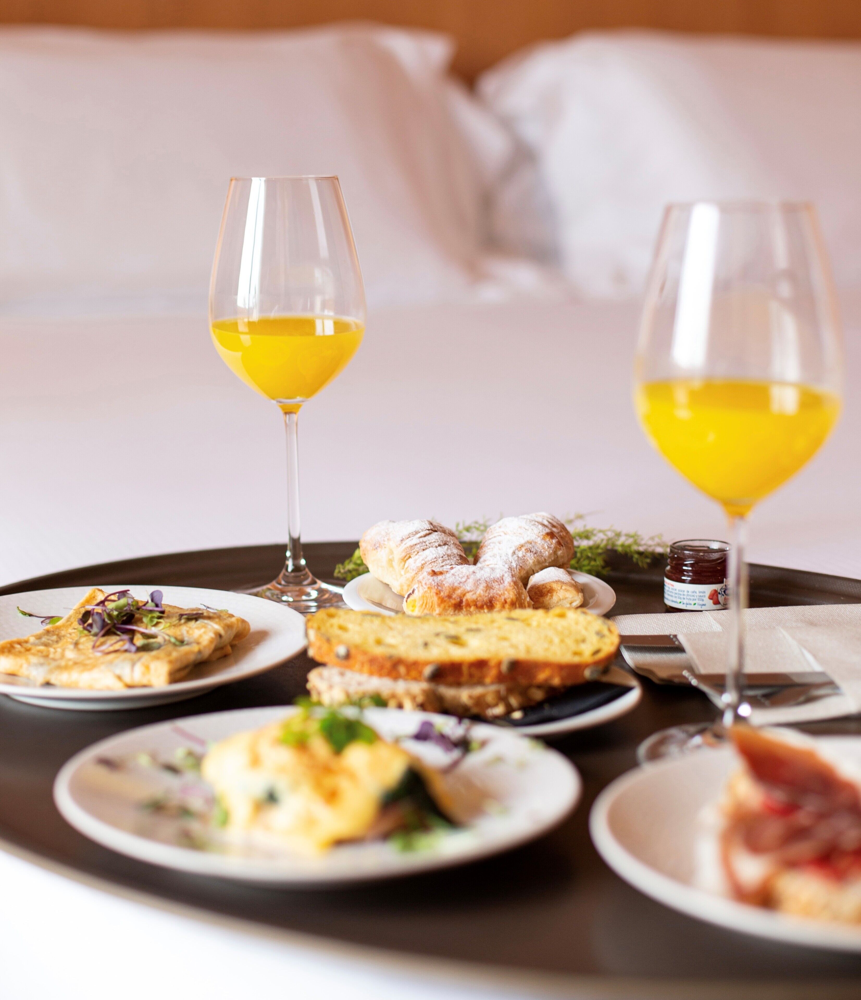 A breakfast tray with pastries, bread, and a croissant, accompanied by two glasses of orange juice.