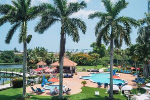 A resort pool area with palm trees, lounge chairs, and umbrellas. - Hilton Palm Beach PBI (West Palm Beach)