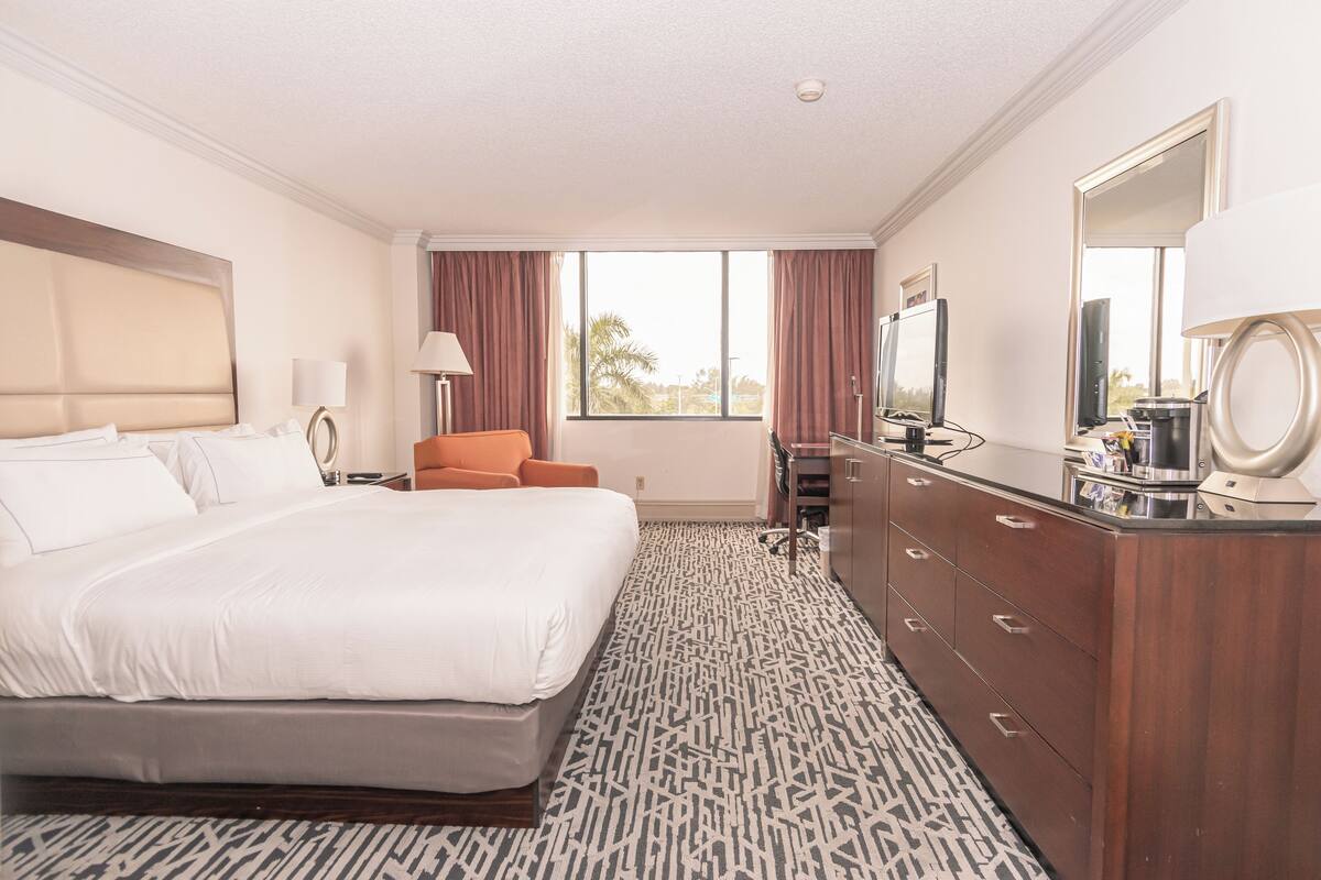 Une chambre d’hôtel avec un grand lit, une commode en bois, un bureau avec un ordinateur et une télévision.