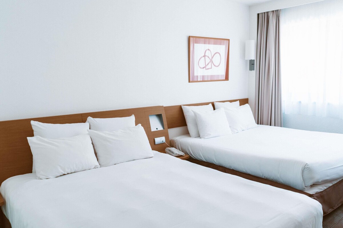 Two single beds with wooden headboards, white bedding, a framed picture on the wall, and a window with curtains.