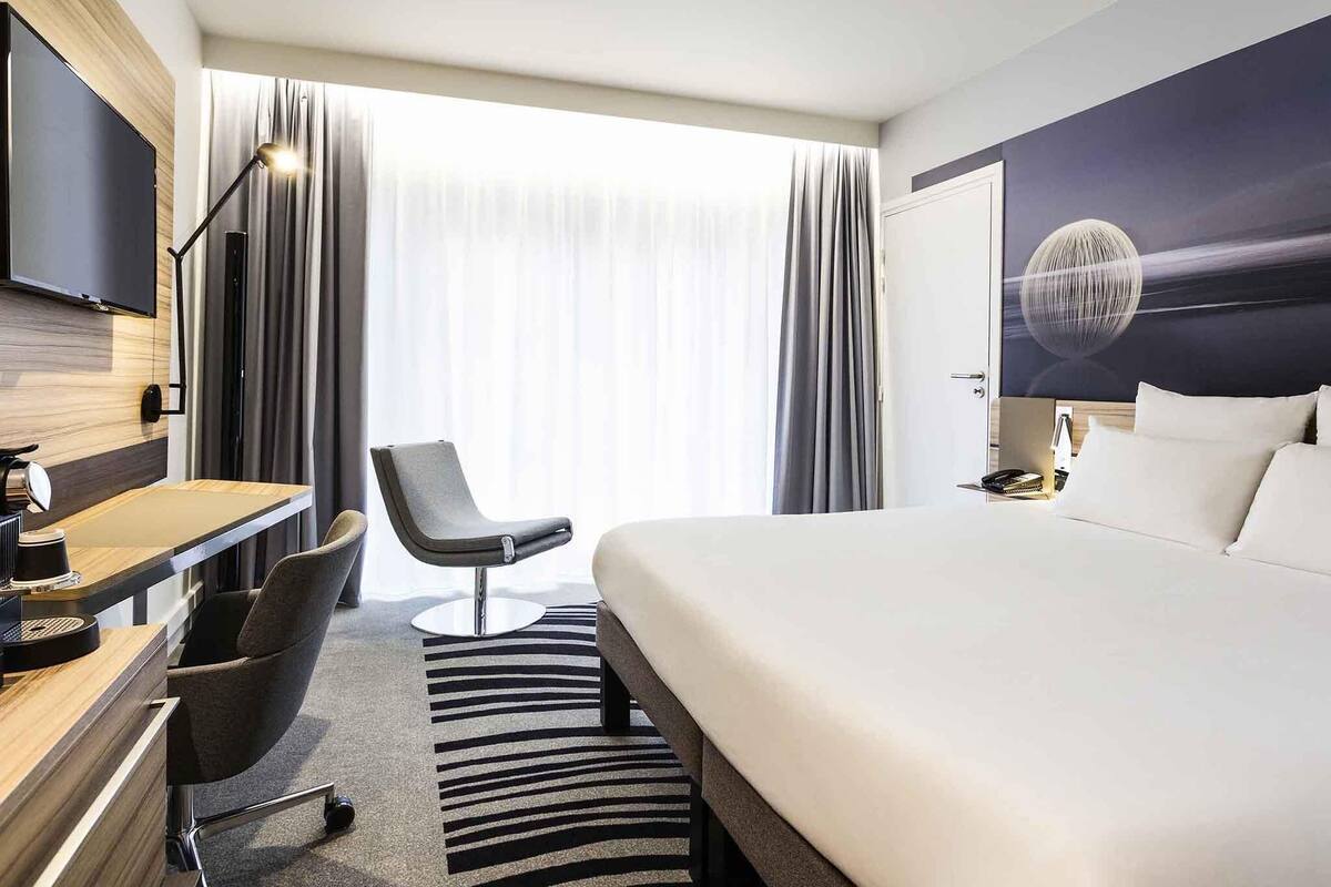 Habitación de hotel moderna con una cama grande, un escritorio con silla, televisión y vistas al exterior.