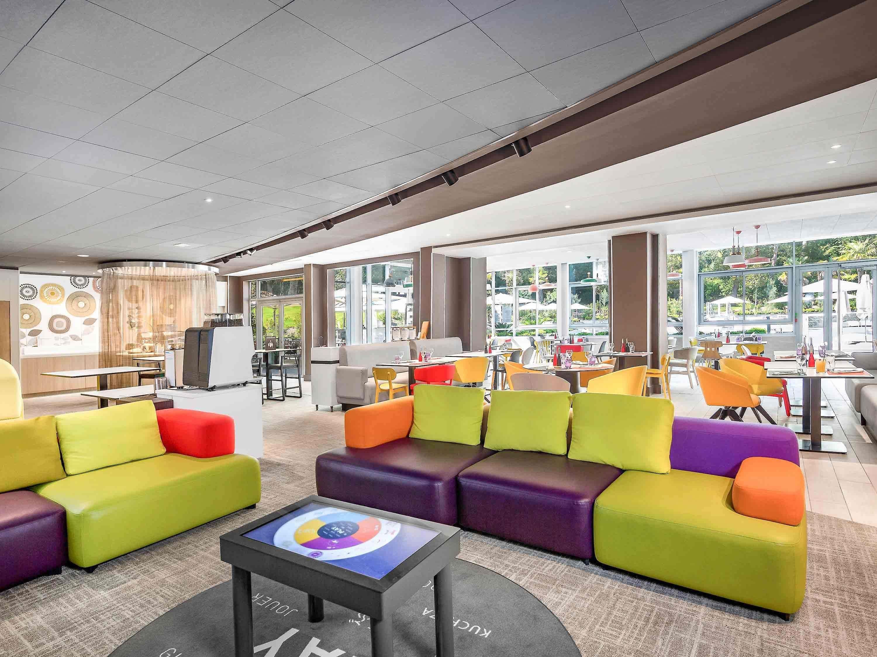 En modern hotellobby med färgglada sittmöbler, en kaffebar och stora fönster som ger utsikt över omgivningarna.
