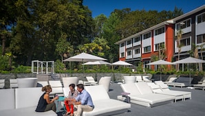 A rooftop lounge area with white lounge chairs and umbrellas, surrounded by greenery and a modern building. - Novotel Resort & Spa Biarritz Anglet (Anglet)