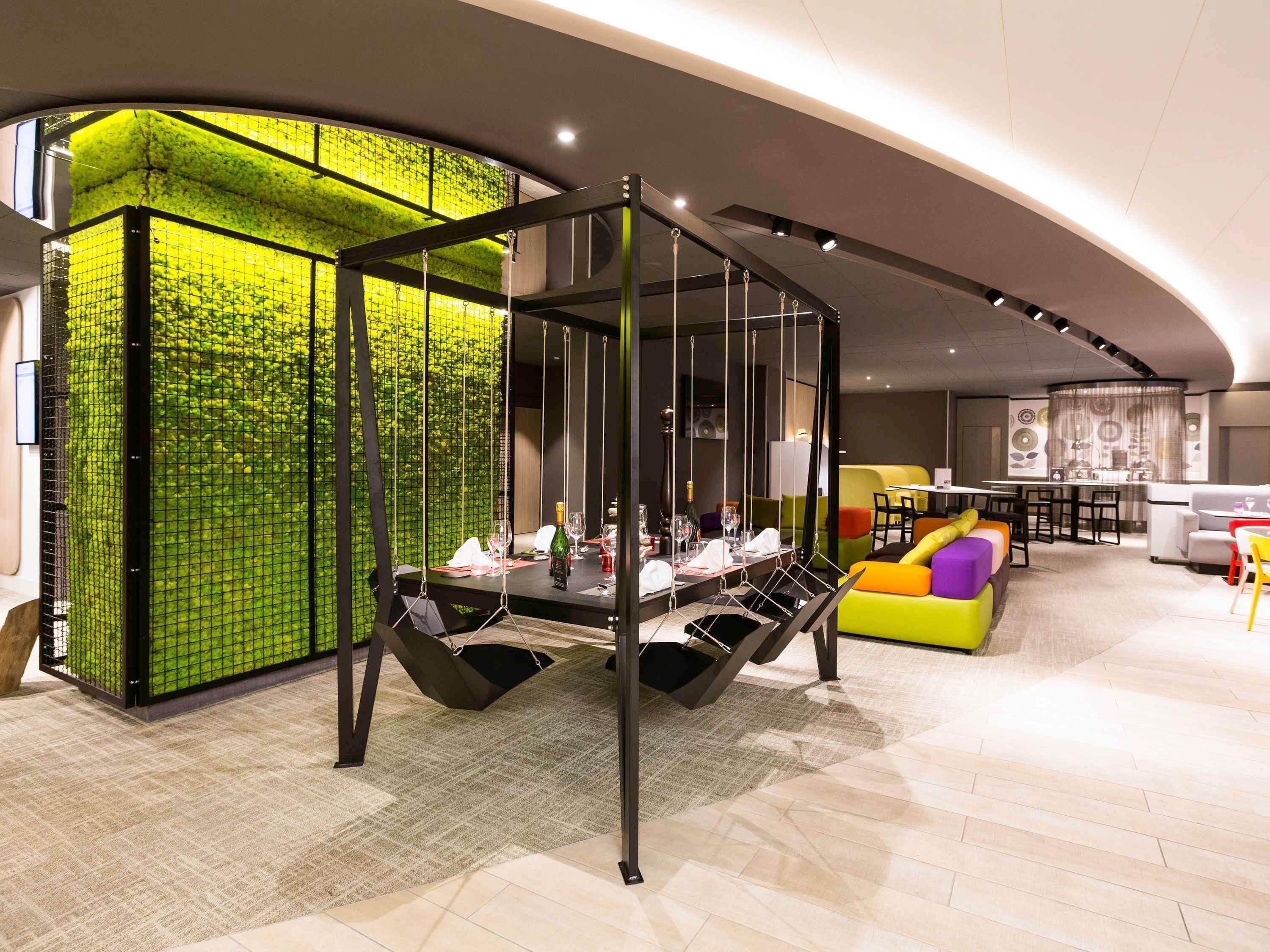 A modern interior with a dining area featuring a unique hanging chair and a vibrant green wall.